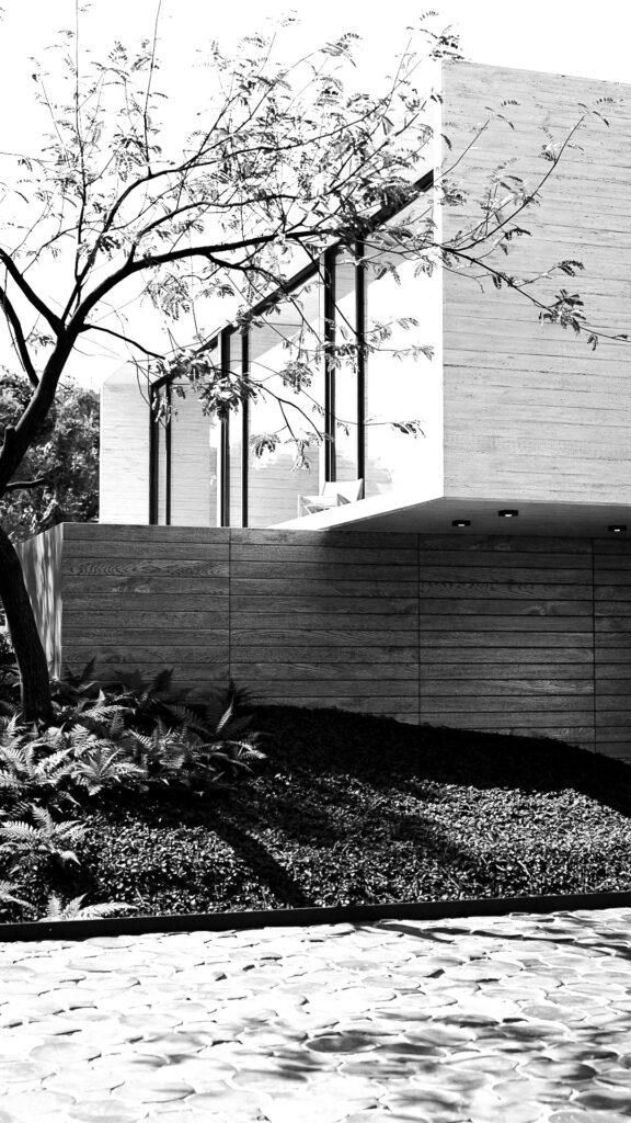 "Fachada principal de Casa Blanco con volumen flotante de concreto y muros de madera"