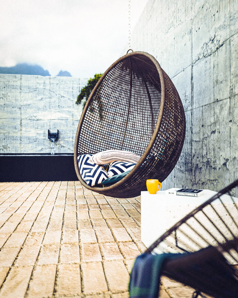 "Terraza exterior de concreto con silla colgante y vista a las montañas"