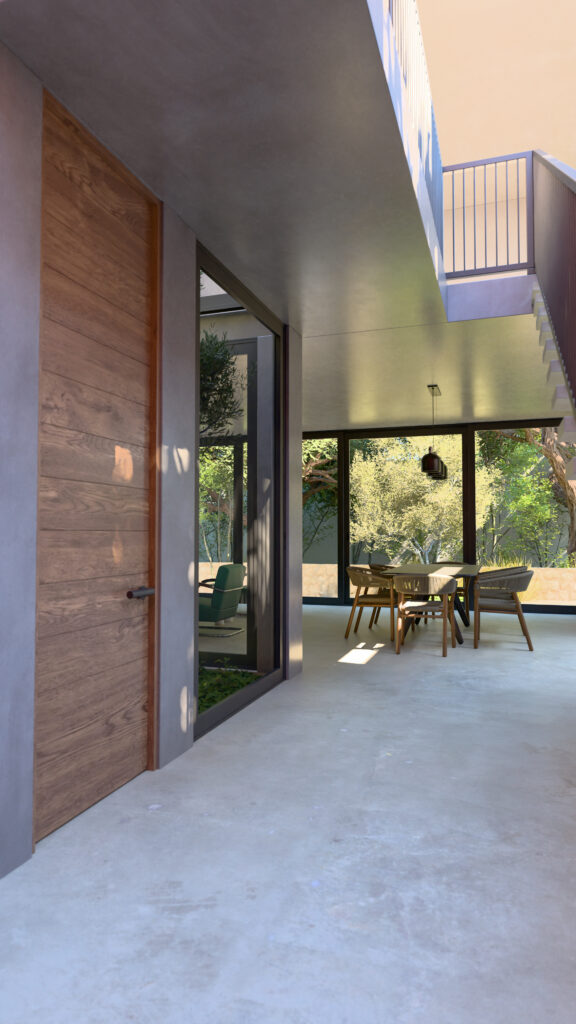 Pasillo de transición interior-exterior con pisos de concreto y muros de cristal hacia el patio central